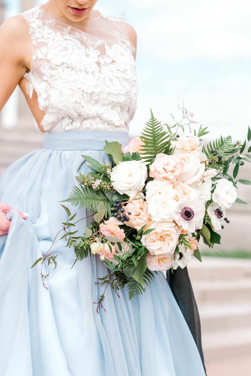 Bride with light blue wedding skirt holding blush and peach bouquet with black ribbon